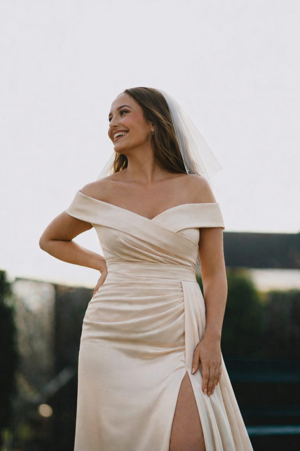 Bride wearing an off-the-shoulder satin wedding dress with a thigh slit, styled for a modern ceremony