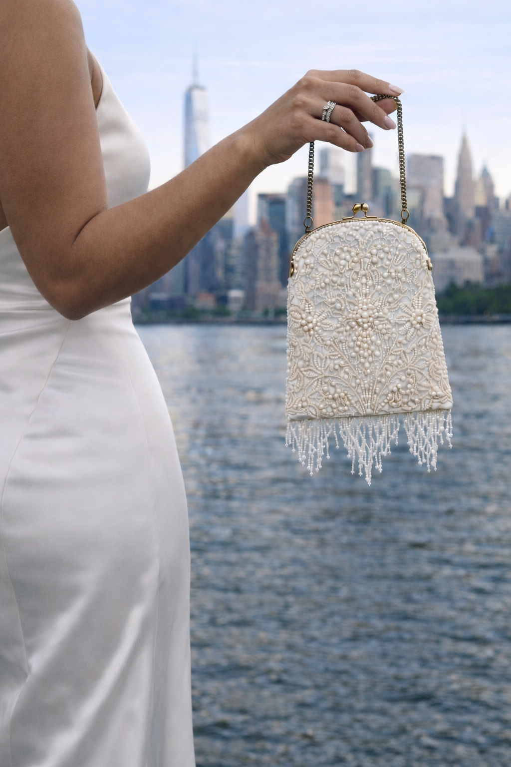 Bride in a satin wedding dress holding a beaded and embroidered bridal bag with a city skyline in the background