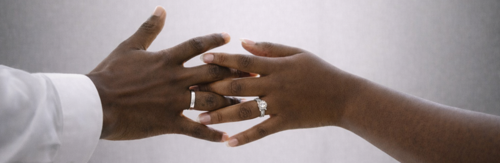 Close-up of hands wearing a moissanite engagement ring and a modern wedding band